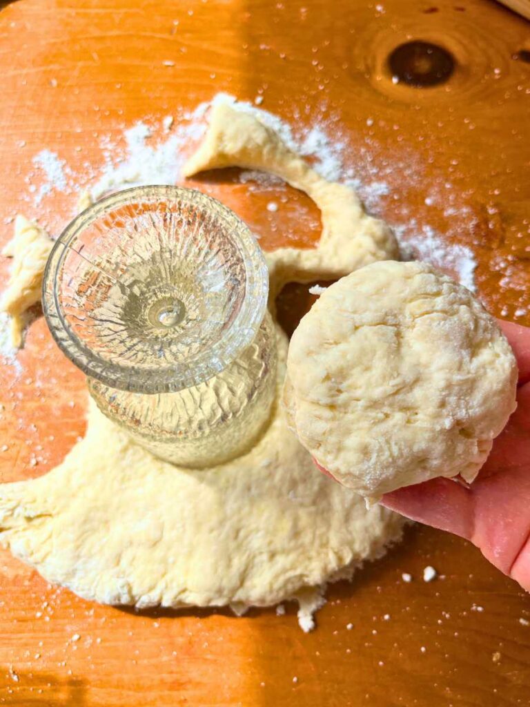 A glass cup pressed into scone dough. A woman is holding a dough scone in her hand.