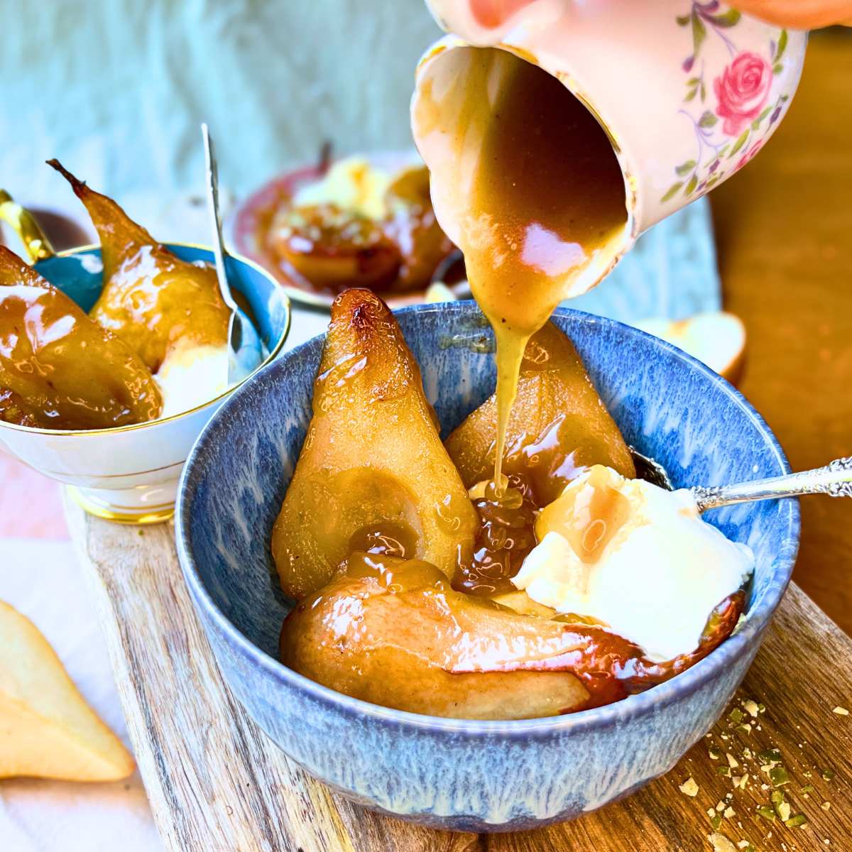A woman pouring caramel sauce onto baked pears in a blue bowl.