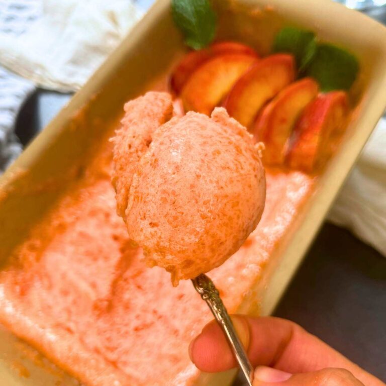 A woman is holding a spoonful of peach sorbet. There is more in the background.