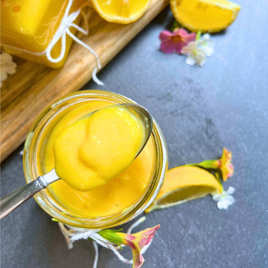 A spoon full of lemon curd is resting on the top of a glass jar.