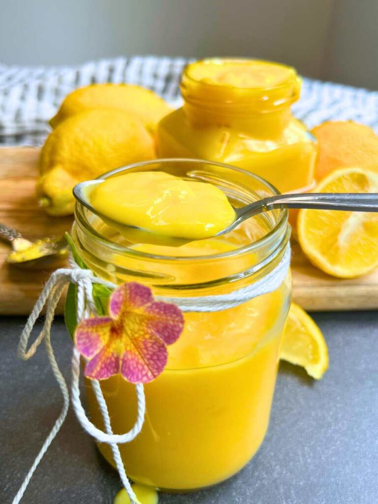 A glass of eggless lemon curd with a spoonful of of lemon curd resting on top.