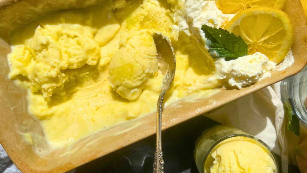 A stone pan with lemon gelato inside. There is whipped cream and sliced lemons at one end.