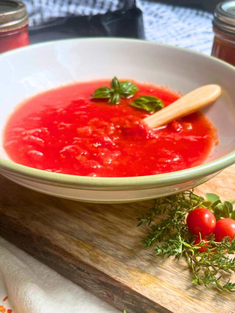 A side view of a bowl of tomato sauce with a wooden spoon inside.
