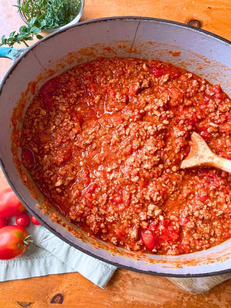 A Dutch oven filled with cooked beef ragu. There is a wooden spoon inside.