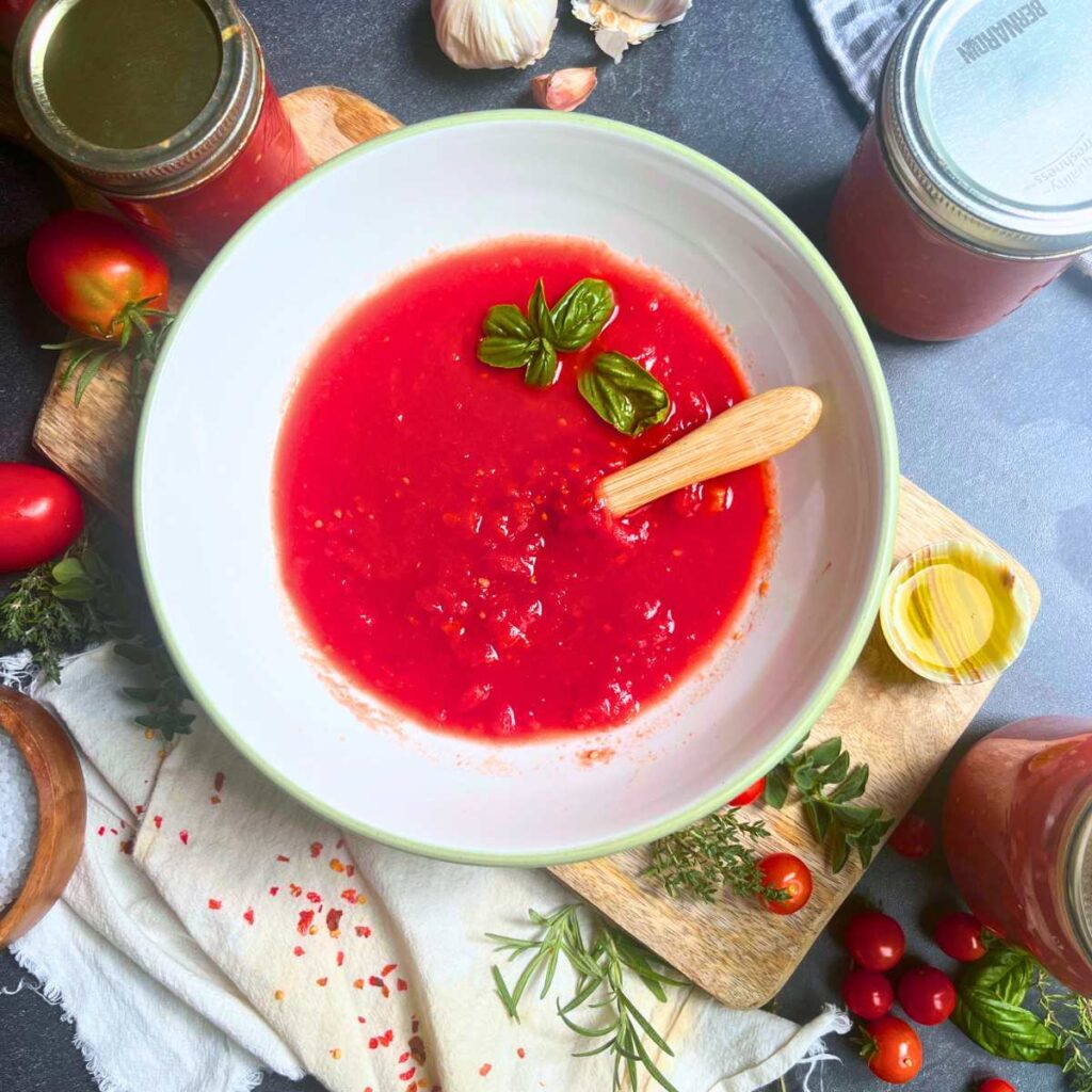 A large white bowl filled with fresh tomato sauce. There is a wooden spoon and fresh basil inside.
