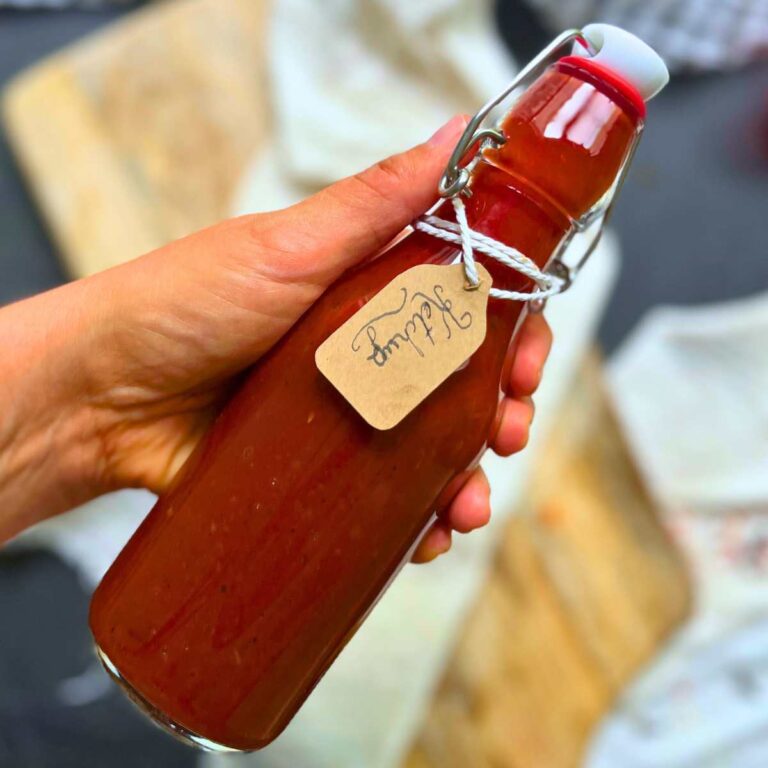 A woman is holding a glass bottle filled with ketchup. It has a brown label on it.