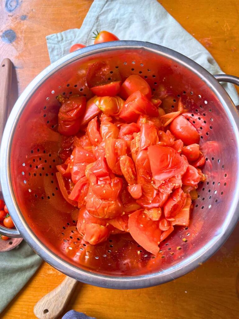 Cooked tomatoes in a metal strainer.