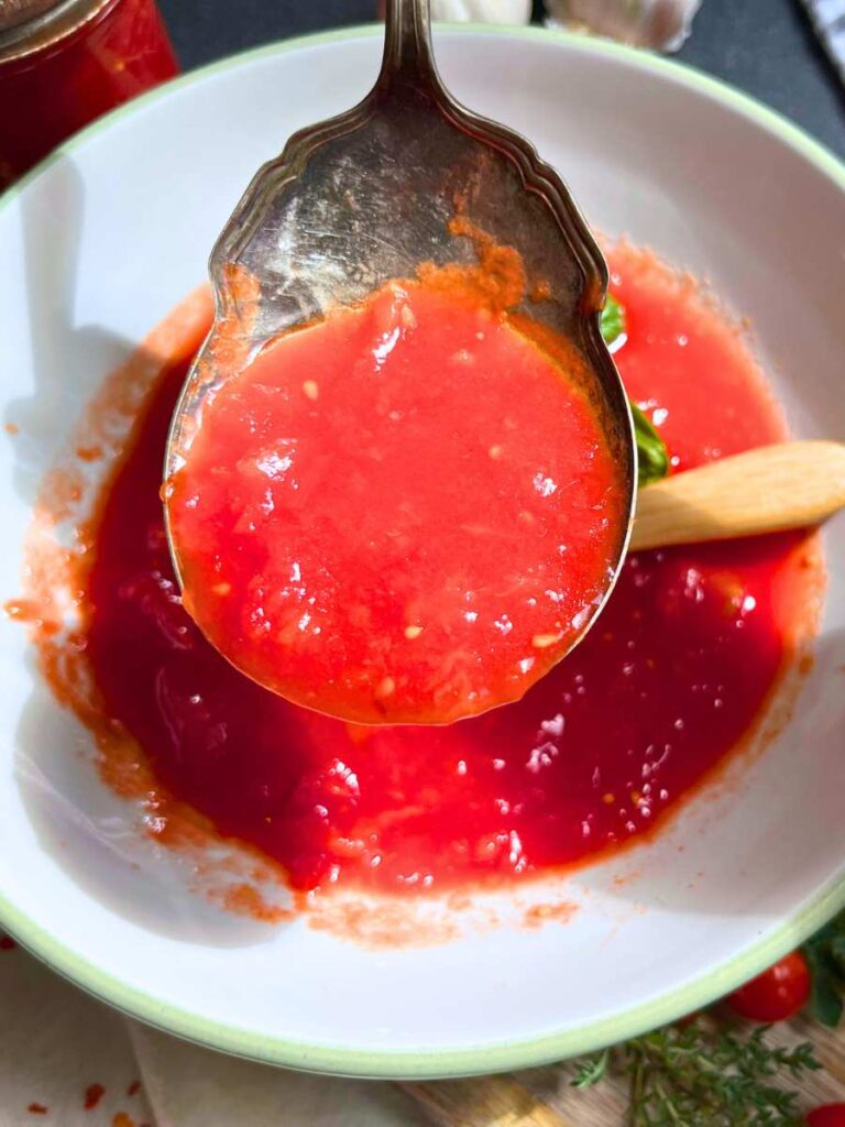 A woman holding a serving spoon of fresh tomato sauce.