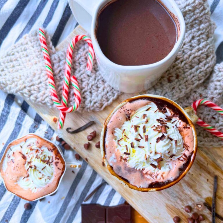 Three mugs of hot chocolate. Two are decorated with whipped cream and shaved chocolate.