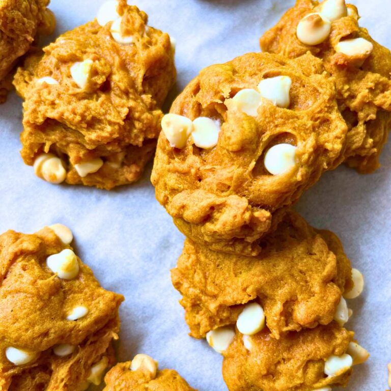 A piece of parchment paper with baked pumpkin cookies with white chocolate chips.
