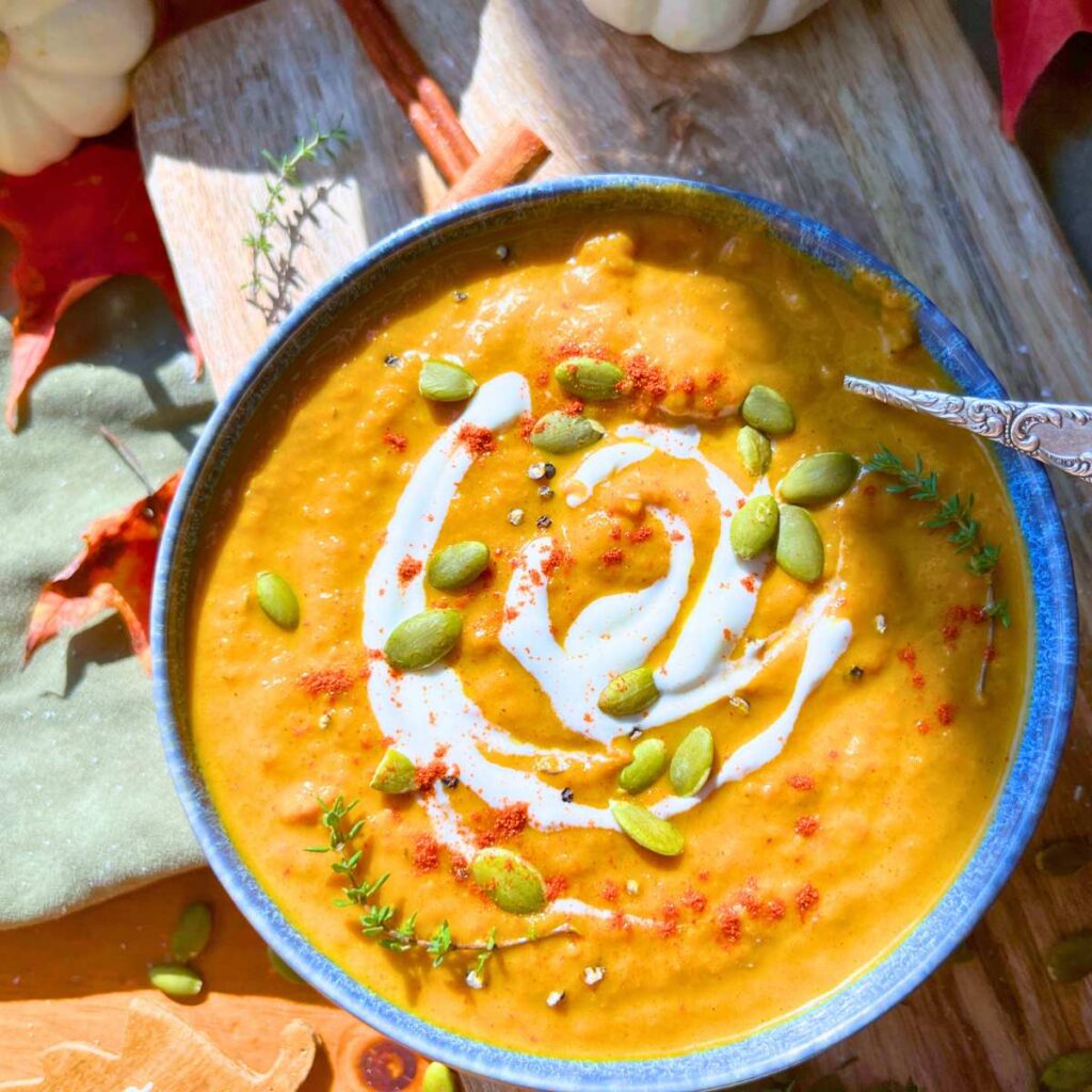 A blue bowl filled with pumpkin soup. There is a swirl of cream on top with pumpkin seeds.