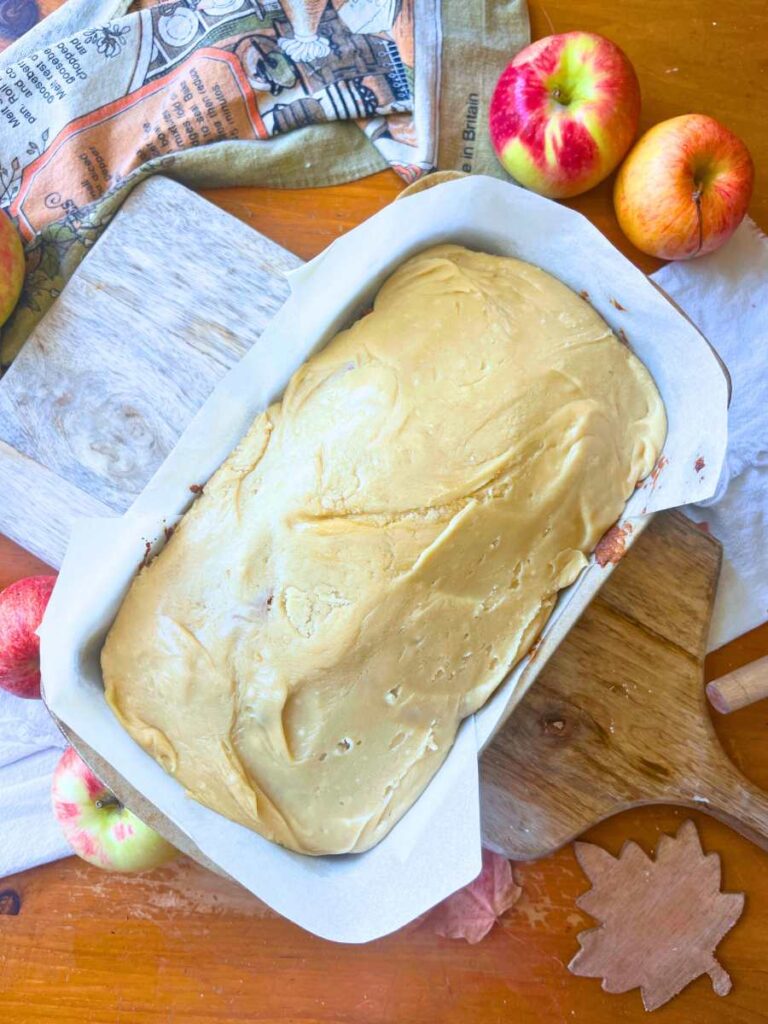 A apple loaf cake in a lined loaf pan with caramel icing spread on top.