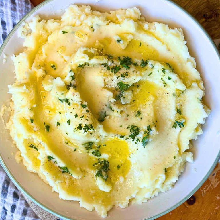 A white bowl of garlic mashed potatoes that are topped with melted butter and parsley.