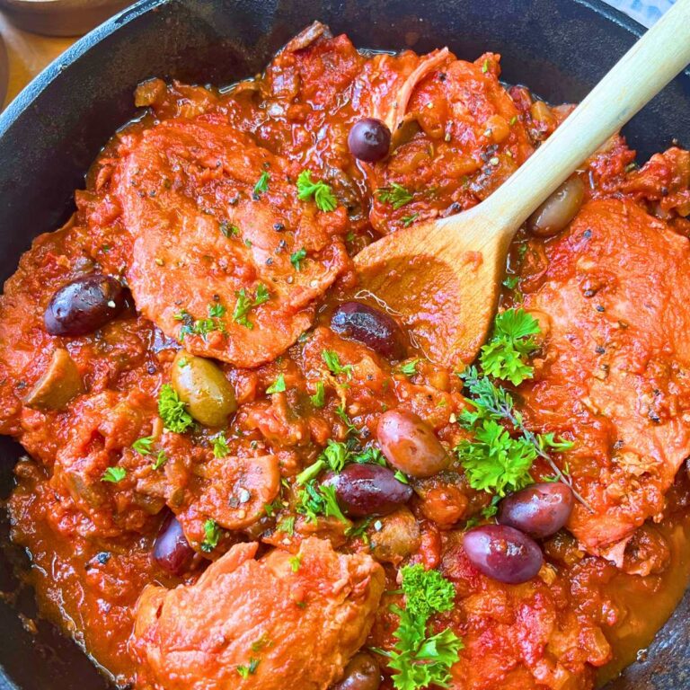 A skillet of chicken cacciatore. There is a wooden spoon inside.