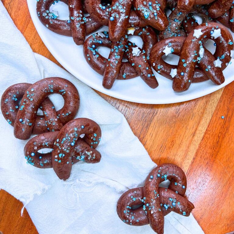 A white plate with chocolate sugar pretzel cookies. There are three cookies off to the side.