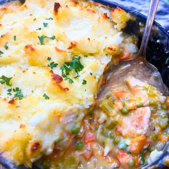 A turkey shepherd's pie in a black casserole dish. Some has been served and a metal serving spoon is inside.
