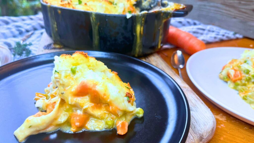 A black plate with a serving of turkey casserole with a mashed potato crust.