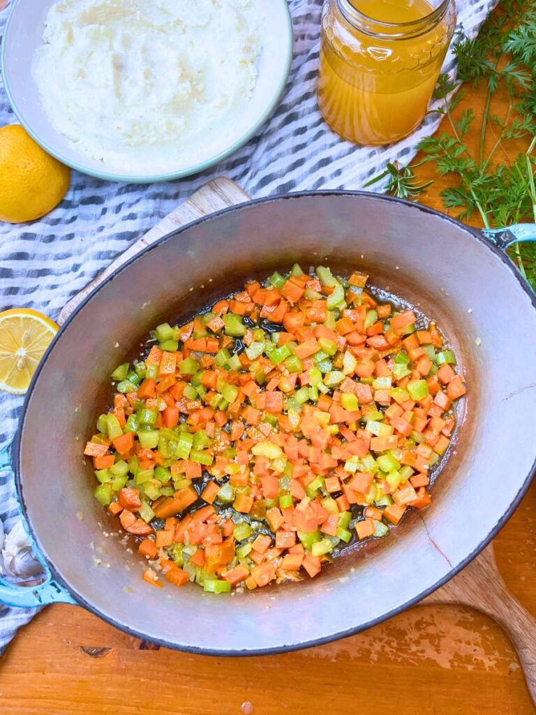 A Dutch oven with diced carrots, onion, and celery inside.