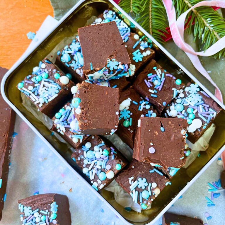 A Christmas tin filled with squares of chocolate fudge. They are decorated with winter themed sprinkles.
