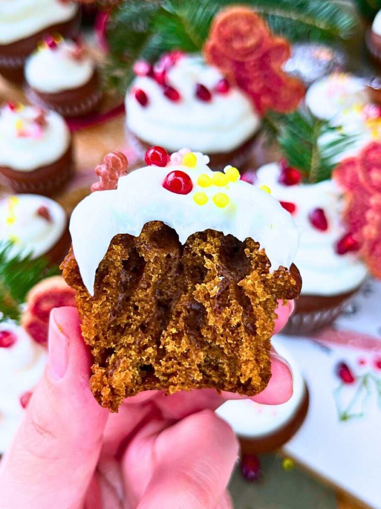 A woman is holding up a mini gingerbread cup cake decorated with festive sprinkles and white icing.