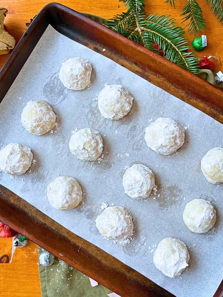 A lined baking sheet filled with powdered snowball cookies.