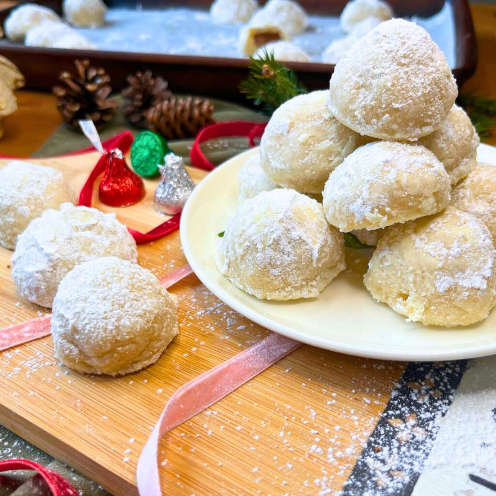 A white plate piled with snowball cookies. There are two off to the side.