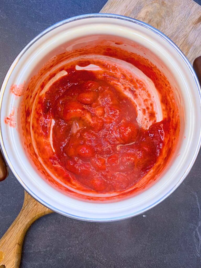 Cooked strawberries in a white sauce pot.