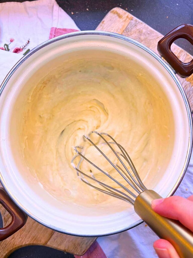 A woman is whisking béchamel in a white sauce pot.