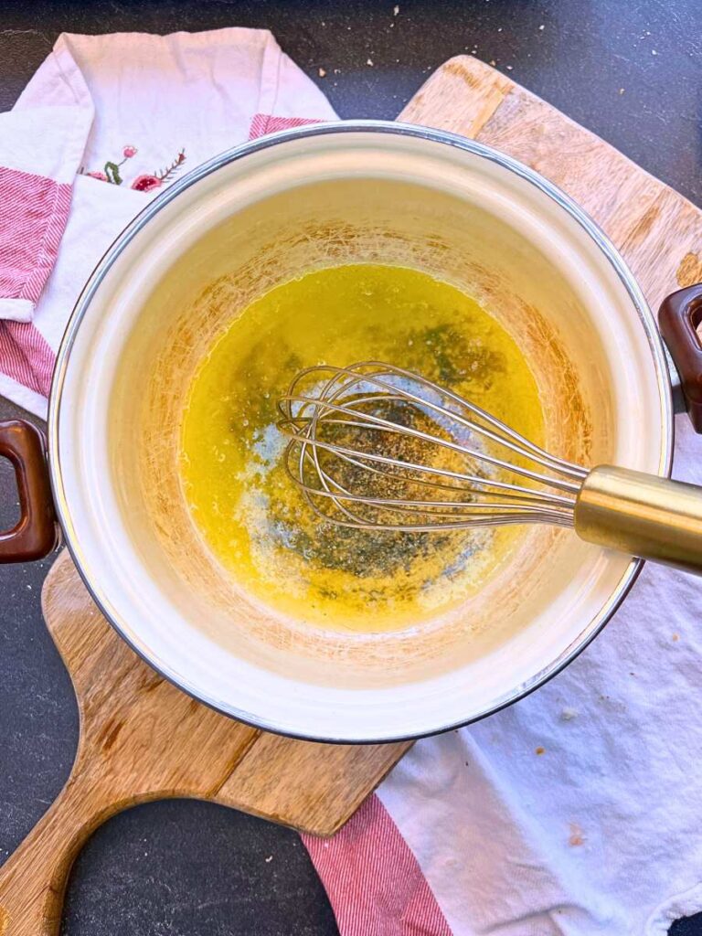 A white sauce pot with melted butter. A woman is whisking it.