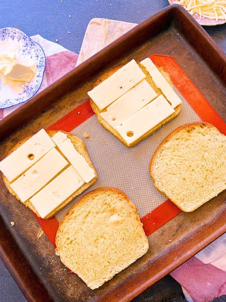 A baking sheet with 4 slices of toast. Half of them are layered with sliced Swiss cheese.
