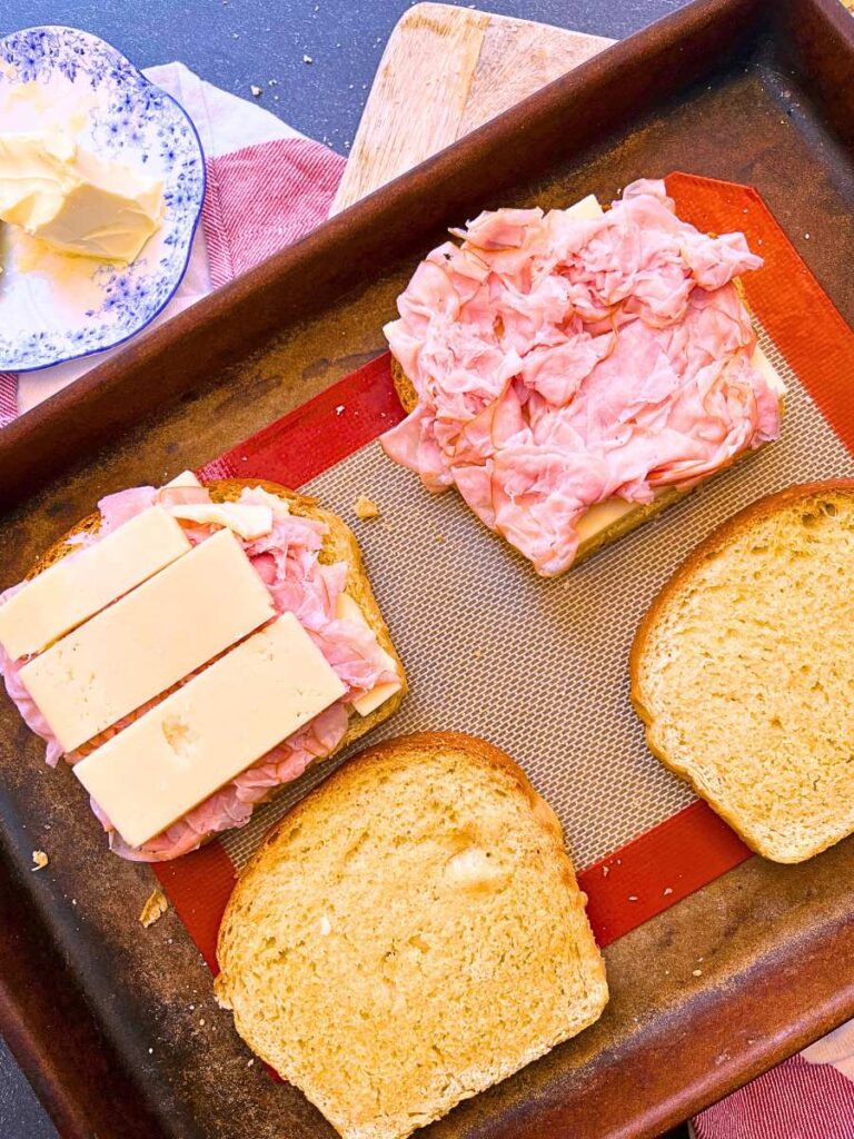 Four slices of toast. Two are layered with Swiss cheeese and ham.