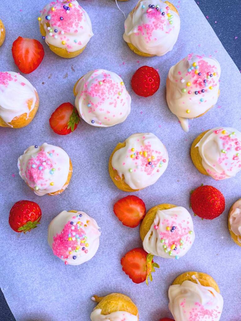 A table full of filled and decorated strawberry profiteroles. There are fresh strawberries arranged around them.