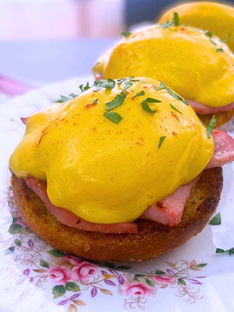 A close up view of an eggs Benedict showing the layers of English muffin, ham, and hollandaise covered poached egg.