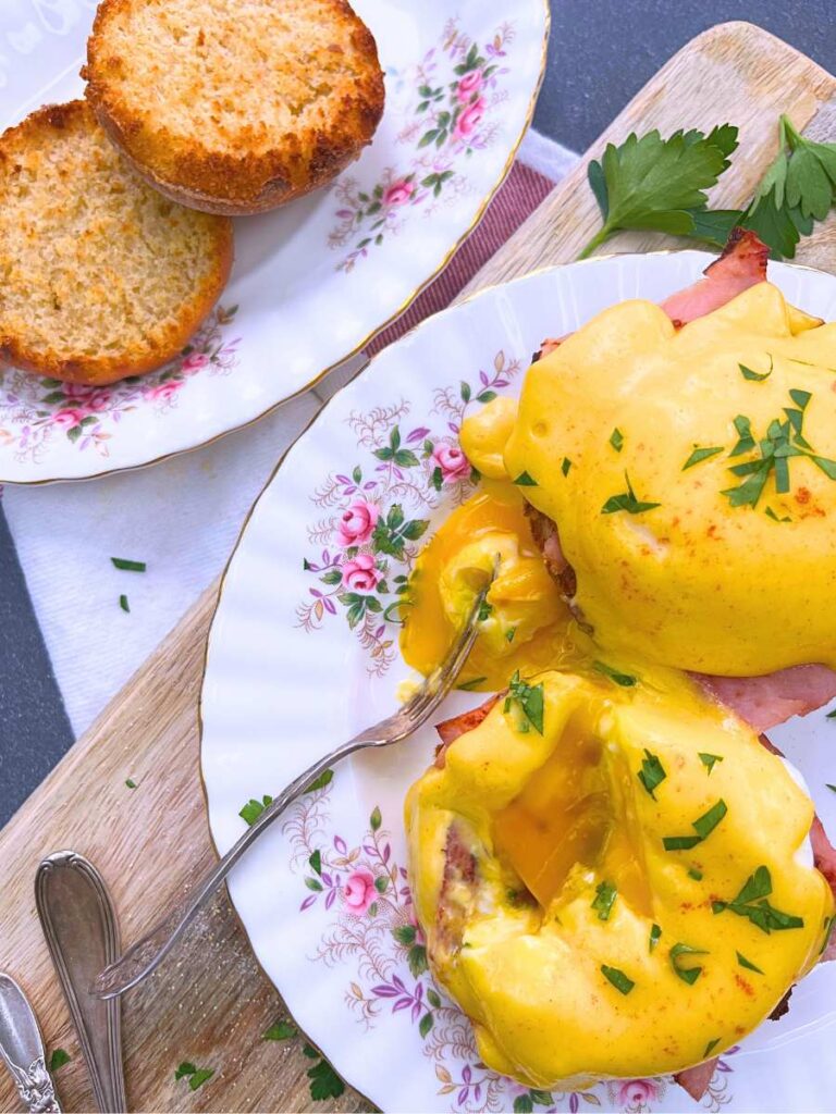 An overhead view of eggs Benedict on a pink floral plate. There is a slice of some egg removed and on a fork.