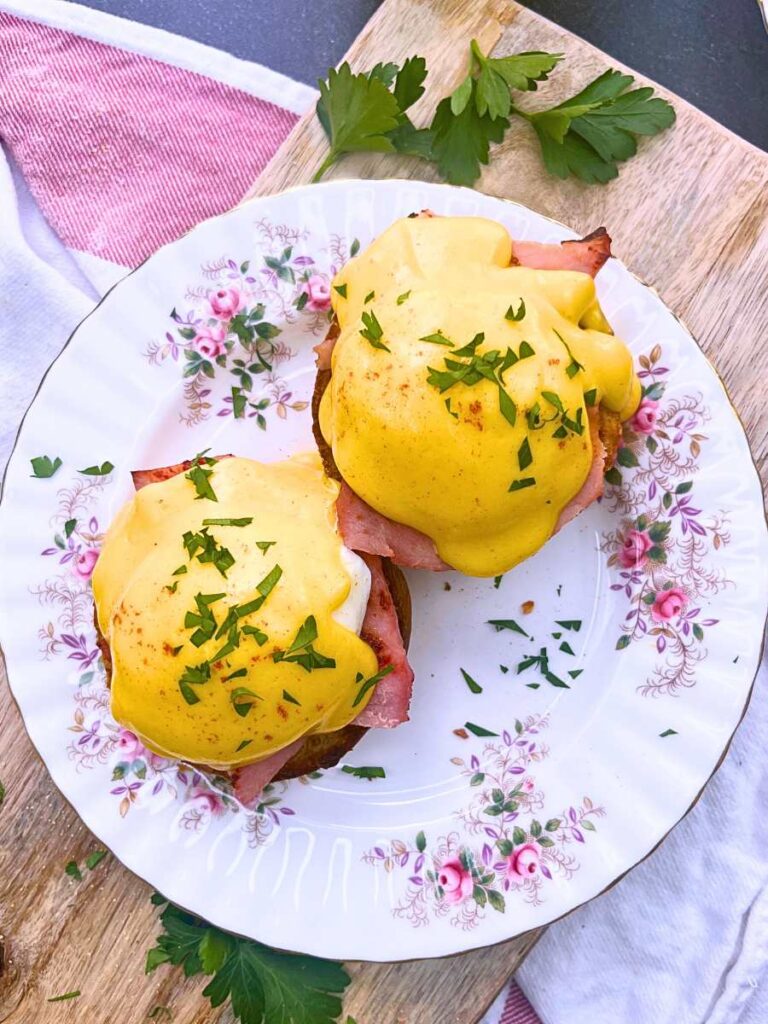 Two garnished eggs Benedict on a pink floral plate.