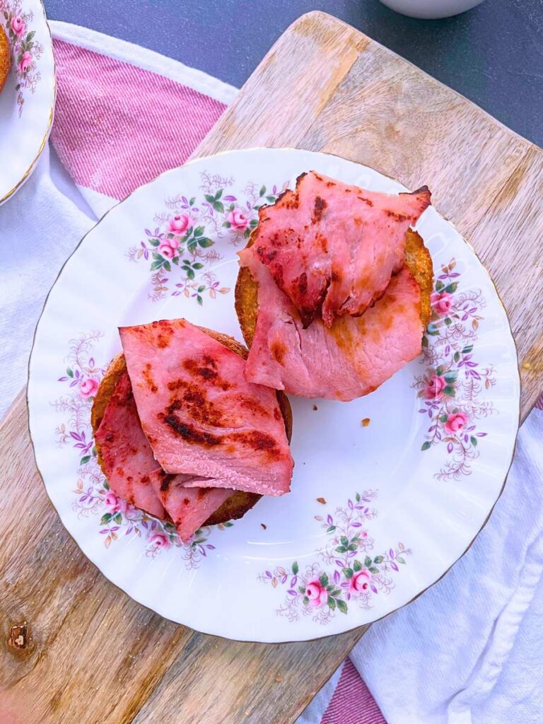 Ham topped English muffins on a pink floral plate.