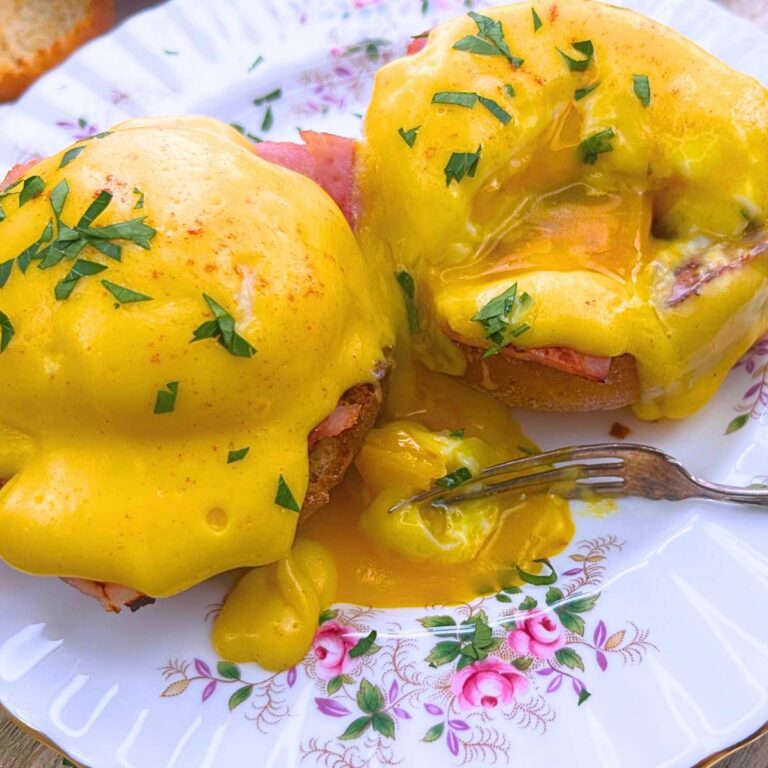 Two eggs Benedict on a pink floral plate. There is a forkful of poached egg in front.