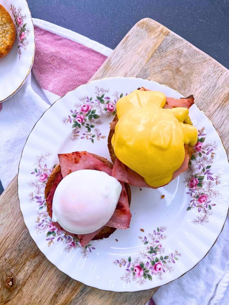 Ham topped English muffins with poached eggs on top. One has hollandaise on top of the egg.