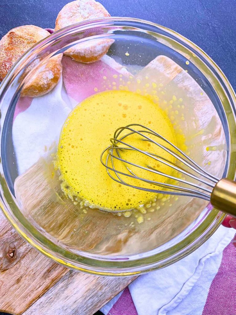 A woman is whisking egg yolks in a glass bowl.