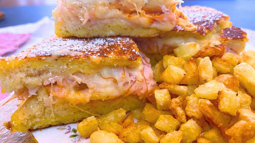 A side view of a sliced Monte Cristo sandwich. There are crispy baked potato cubes in the front.