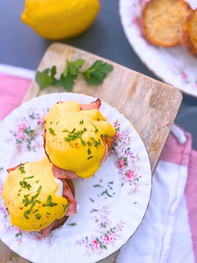Two eggs Benedict on a pink floral plate. They are garnished with chopped parsley.