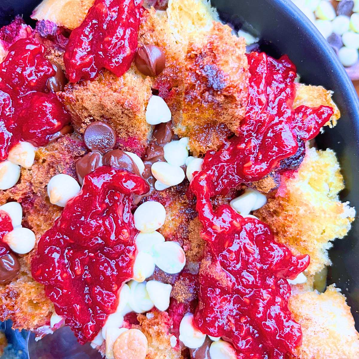 A close up look at the top of a French toast casserole that is topped with raspberry purée and chocolate chips.
