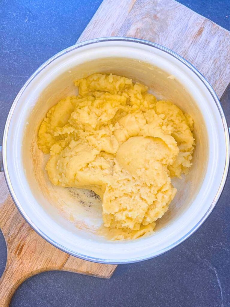 A white sauce pot with cooked dough inside.