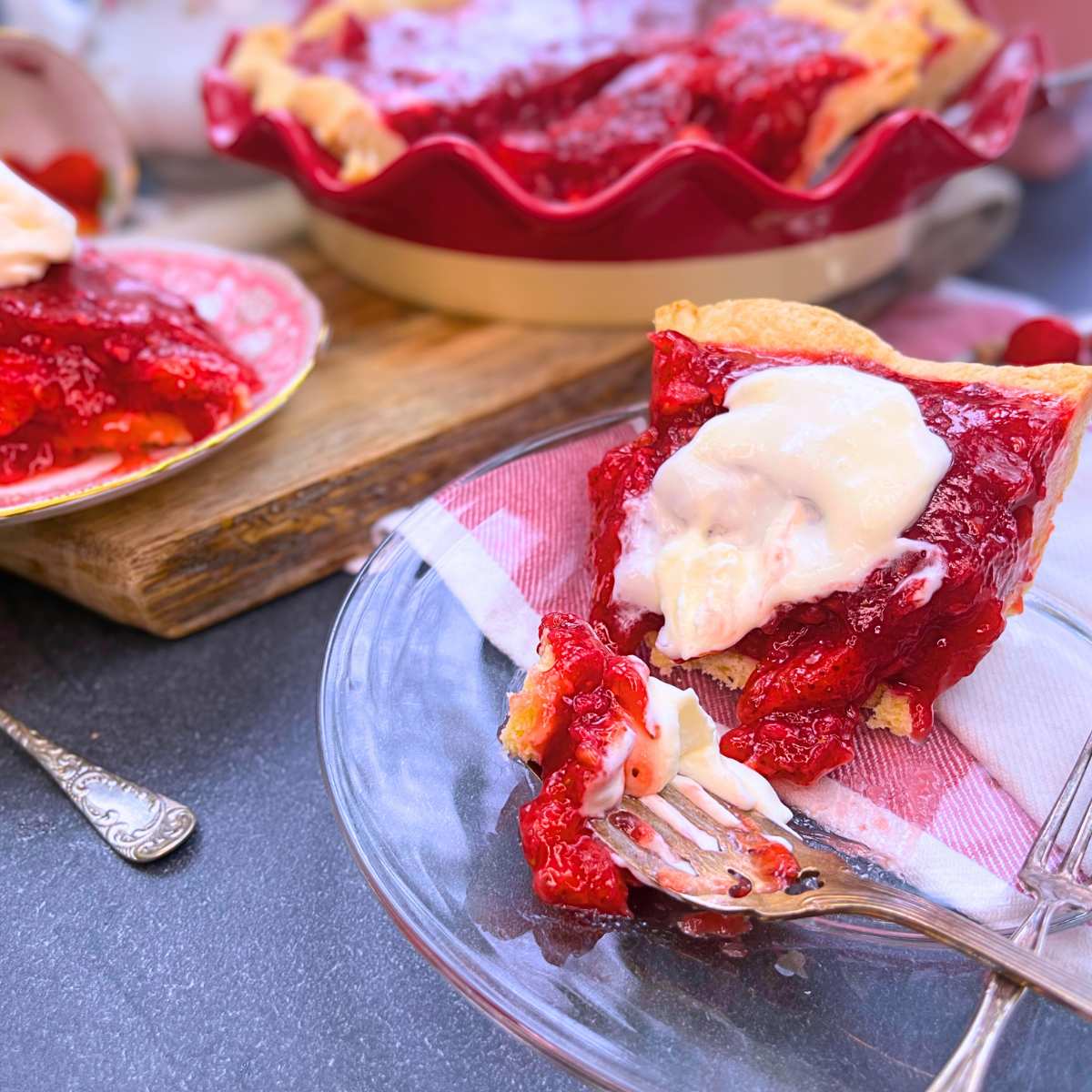 A partially eaten slice of strawberry pie with whipped cream on top. There is more pie in the background.