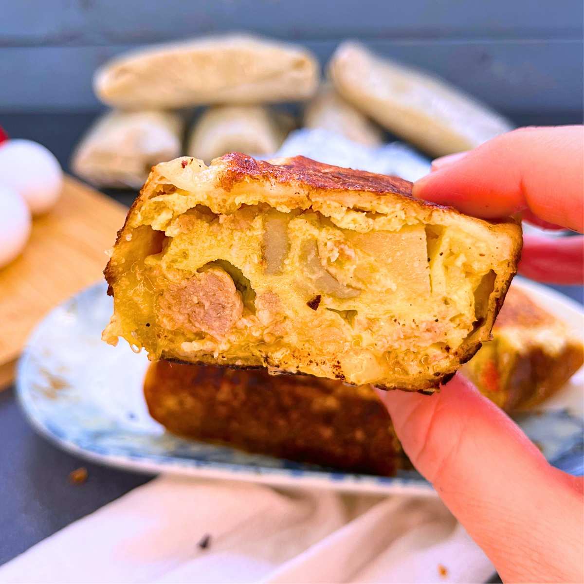 A woman is holding a breakfast wrap that has been cut in half to show the inside filling.