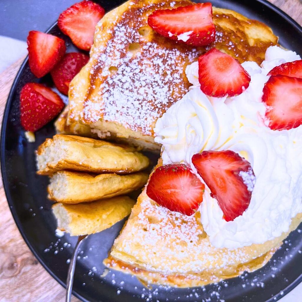 An overhead view of a stack of buttermilk pancakes garnished with whipped cream and strawberries.