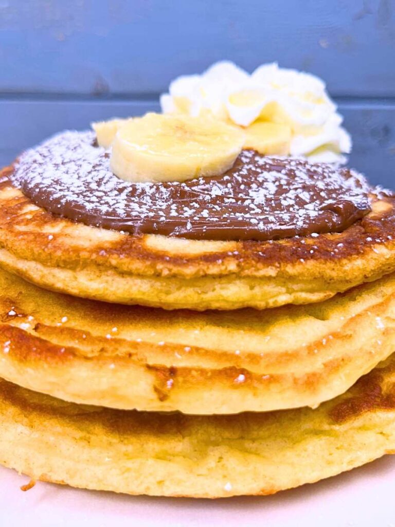 A stack of buttermilk pancakes topped with Nutella and sliced bananas.