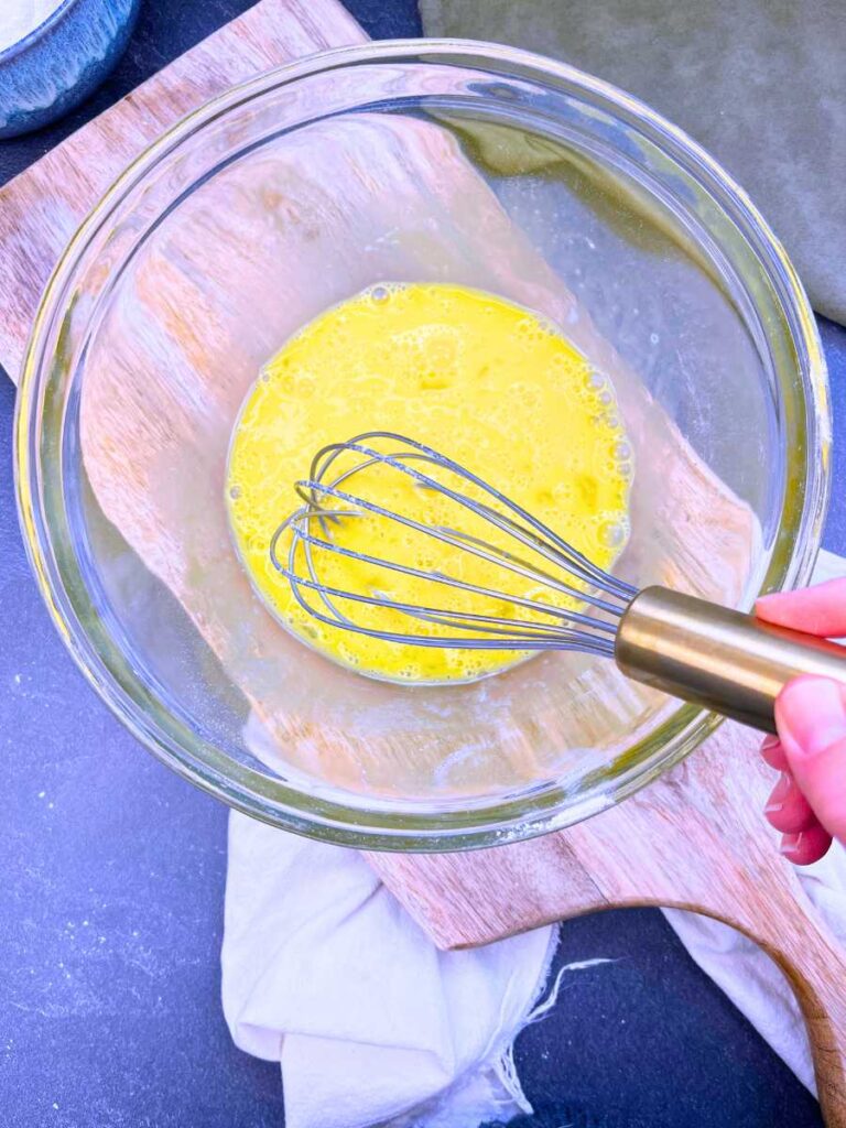 A woman is whisking eggs in a glass bowl.