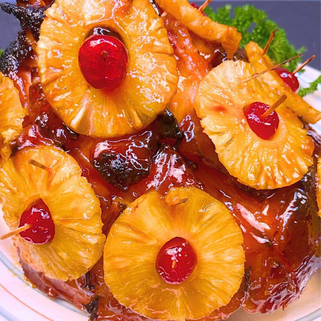 A sude view of an Easter ham glazed and garnished with cooked pineapple rings and maraschino cherries.