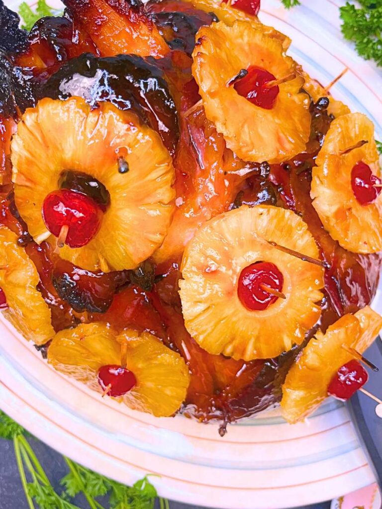 A overhead view of a glazed roasted ham, studded with pineapple rings and maraschino cherries.